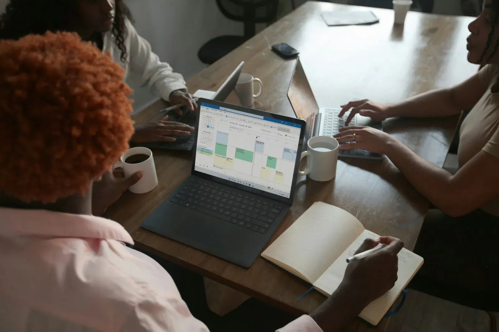 Team planning around a laptop calendar with notebooks and coffee