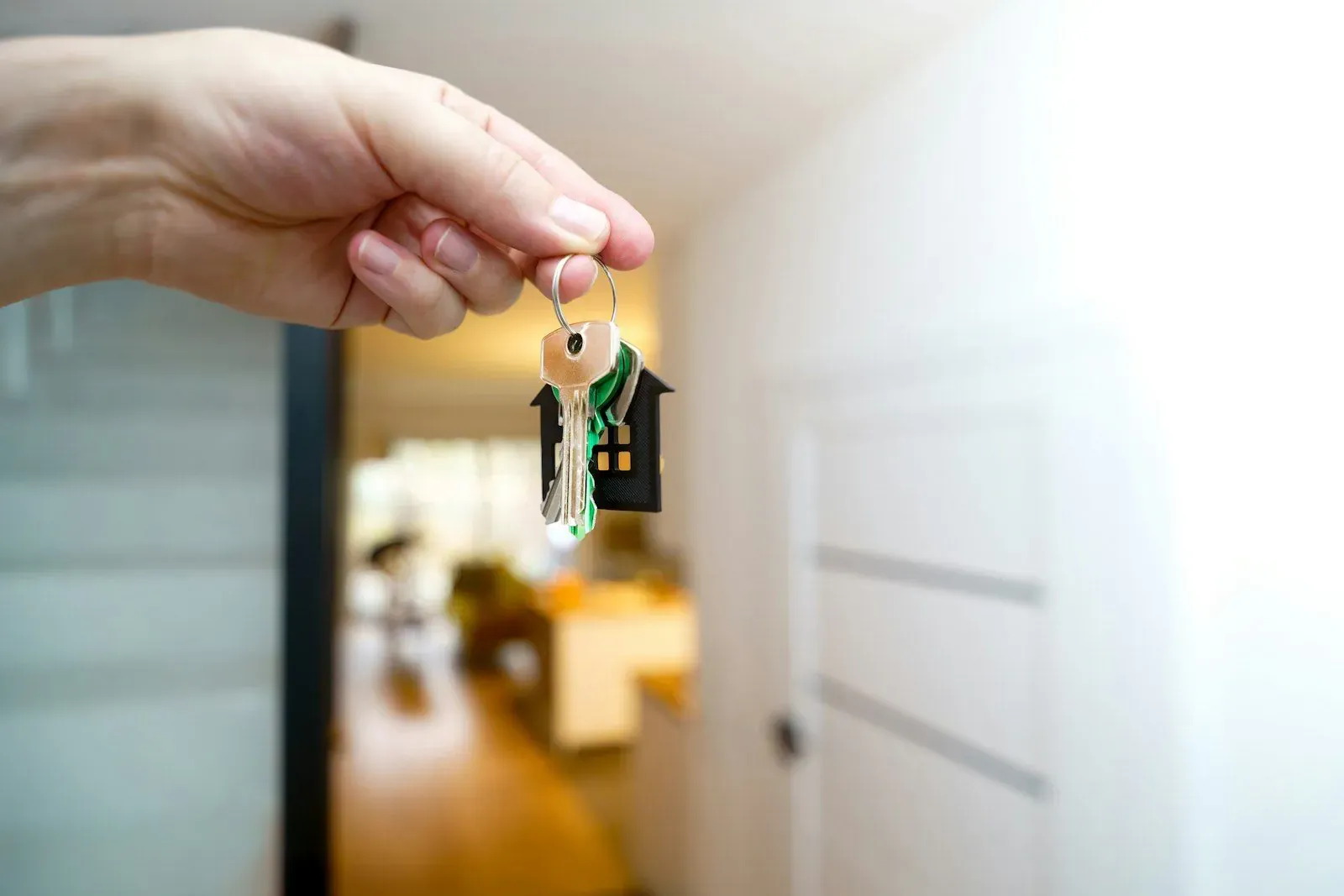 Hand holding house keys with a house-shaped keychain at the entrance